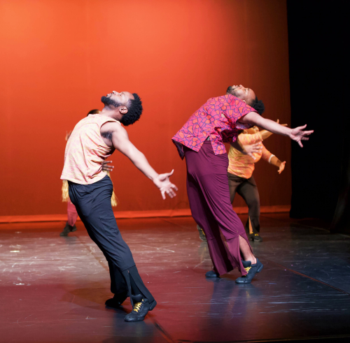 Dancers in front of an orange background. They face sideways, stage right, and do an arching back action.