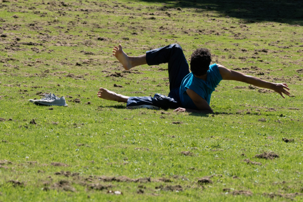 A dancer moving in the grass, posing with right leg and arm in the air.