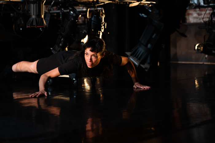 A dancer crawls under lowered stage lighting. 