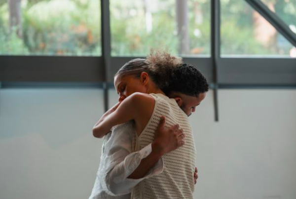 A photo of two dancers embracing. We see their upper bodies.