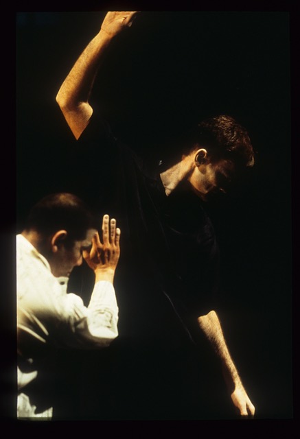 Two dancers in poses, capturing just their upper bodies. One dancer has both arms tilted to make a diagonal line, and one dancer has angular arms bent at the elbows.