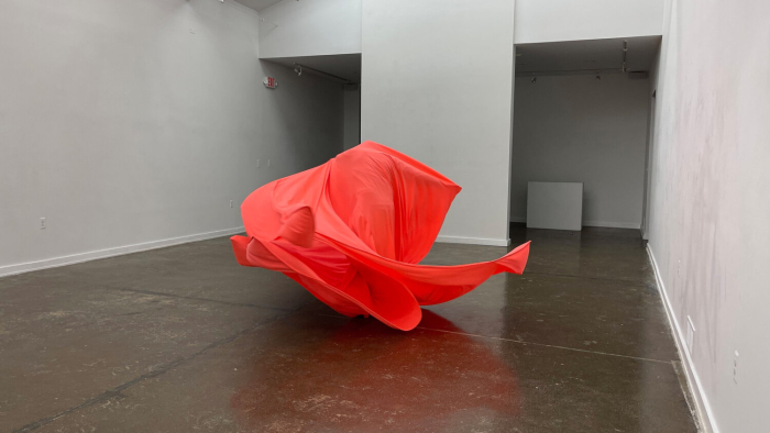 A red fabric sculpture on a concrete floor with white walls.
