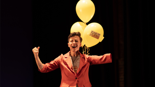 A photo highlights a dancer's upper body. She wears a red blazer, and her arms are frozen in the air. Three yellow helium balloons are behind her.