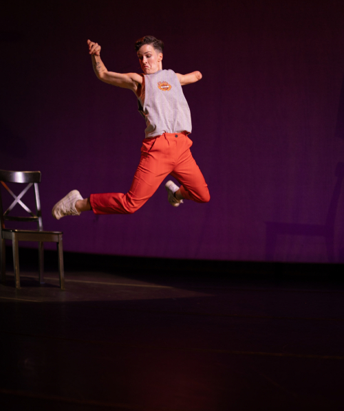 Dancer captured midjump with arms in air and feet kicked towards her backside.