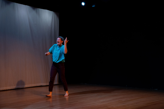 Dancer faces audience with big smile and left hand in the air.