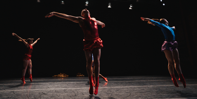 Dancers jump in the air in shiny lamé costumes in front of a black background. Dancers jump in the air in shiny lamé costumes in front of a black background.