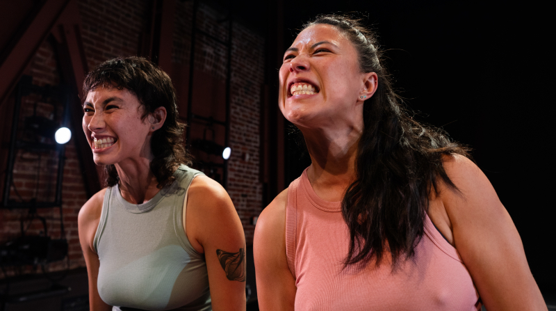A close up of two dancers and their upper bodies. They make faces, showing their teeth and clenching. A close up of two dancers and their upper bodies. They make faces, showing their teeth and clenching.