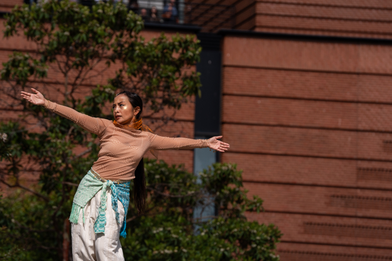 A dancer poses, slightly learning with her arms outstretched.